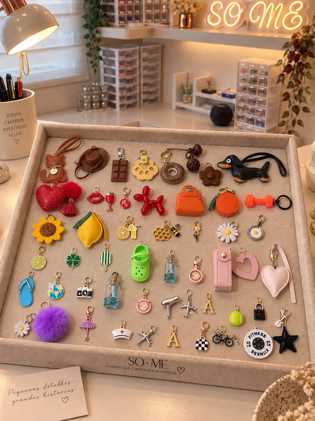 Bandeja do ateliê SO ME com coleção de charms variados sobre mesa clara